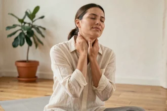 Femme pratiquant un automassage du cou avec les doigts, assise sur un tapis de yoga dans un studio minimaliste