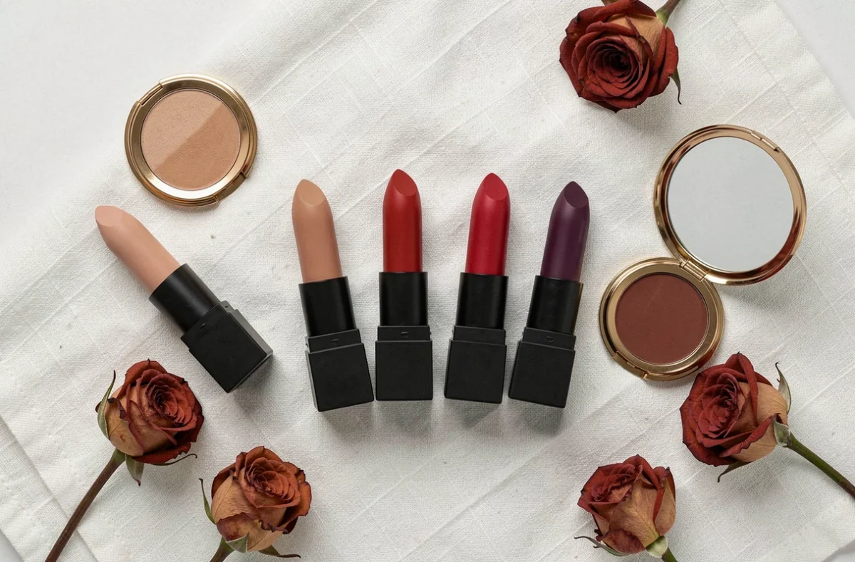 Sélection de rouges à lèvres mats en différentes teintes disposés en flat lay sur fond de lin blanc avec pétales de rose séchées