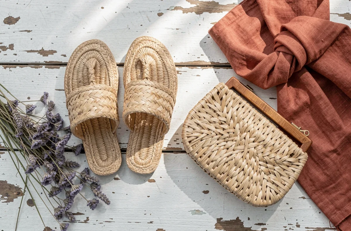 Sandales et pochette en raphia stylisées en flat lay avec accessoires de mode printanière sur bois blanc