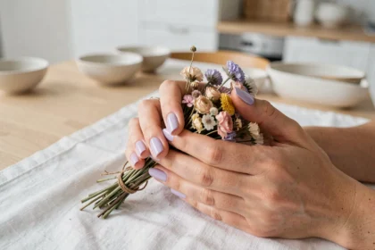 Mains de femme avec vernis à ongles pastel lavande tenant un bouquet de fleurs séchées dans une cuisine scandinave minimaliste